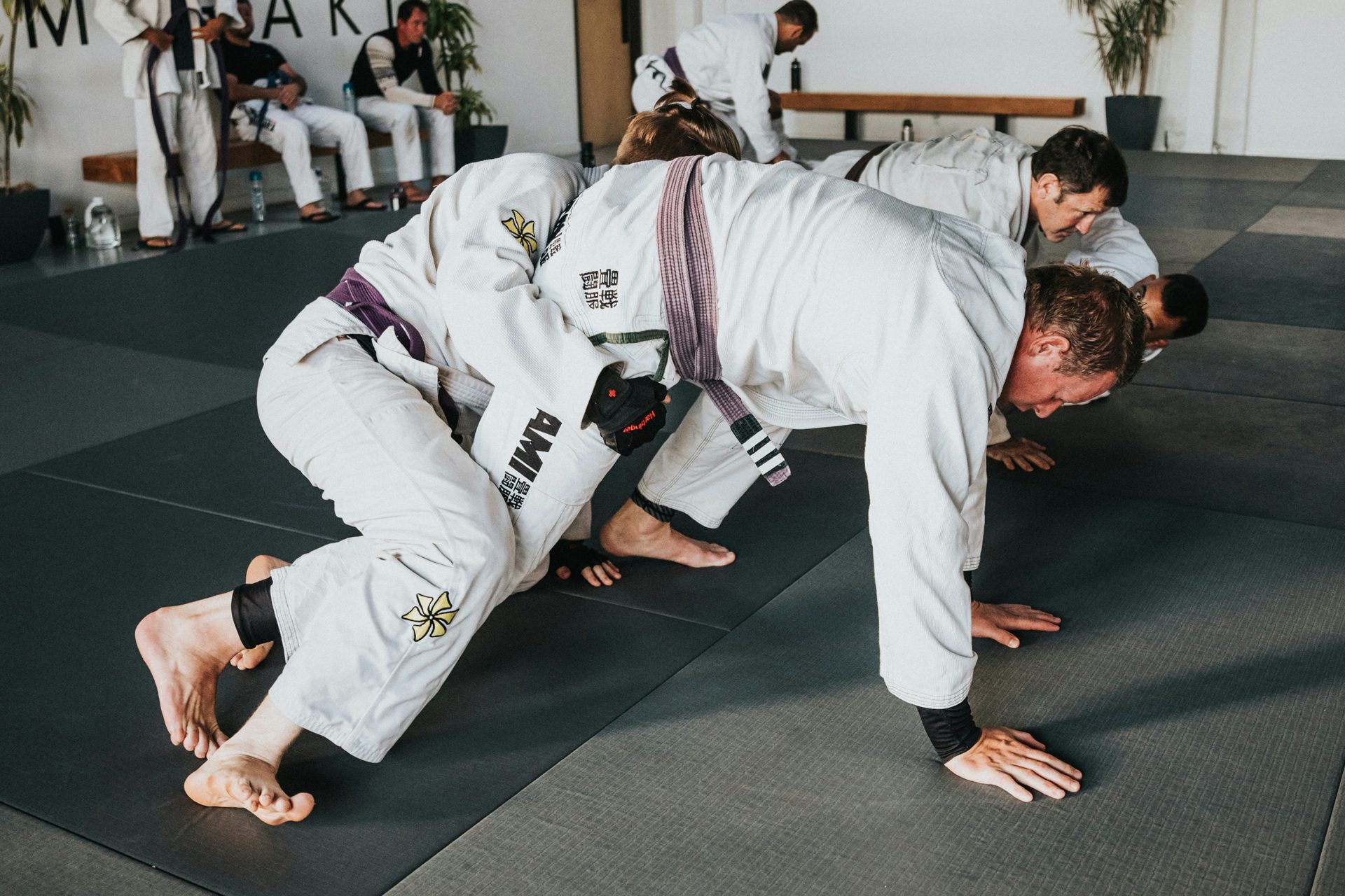 A man in a white and black uniform executes a Brazilian Jiu-Jitsu move on a training mat A man in a white and black uniform executes a Brazilian Jiu-Jitsu move on a training mat
